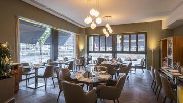 A restaurant with tables set for dining, large windows, and hanging pendant lights.