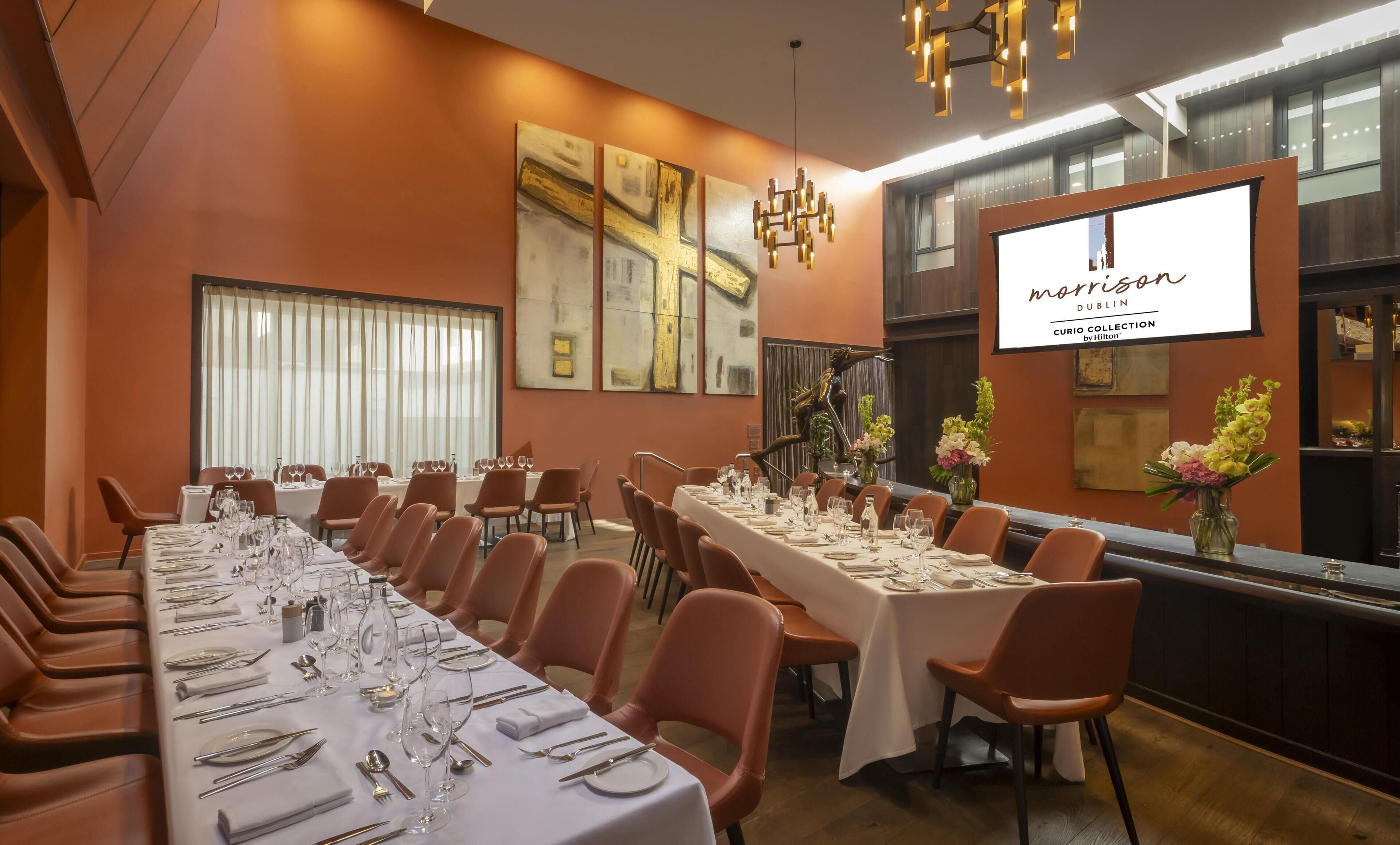 A conference room with long tables set for dining, large windows, and a screen displaying 'Morris Dublin'.