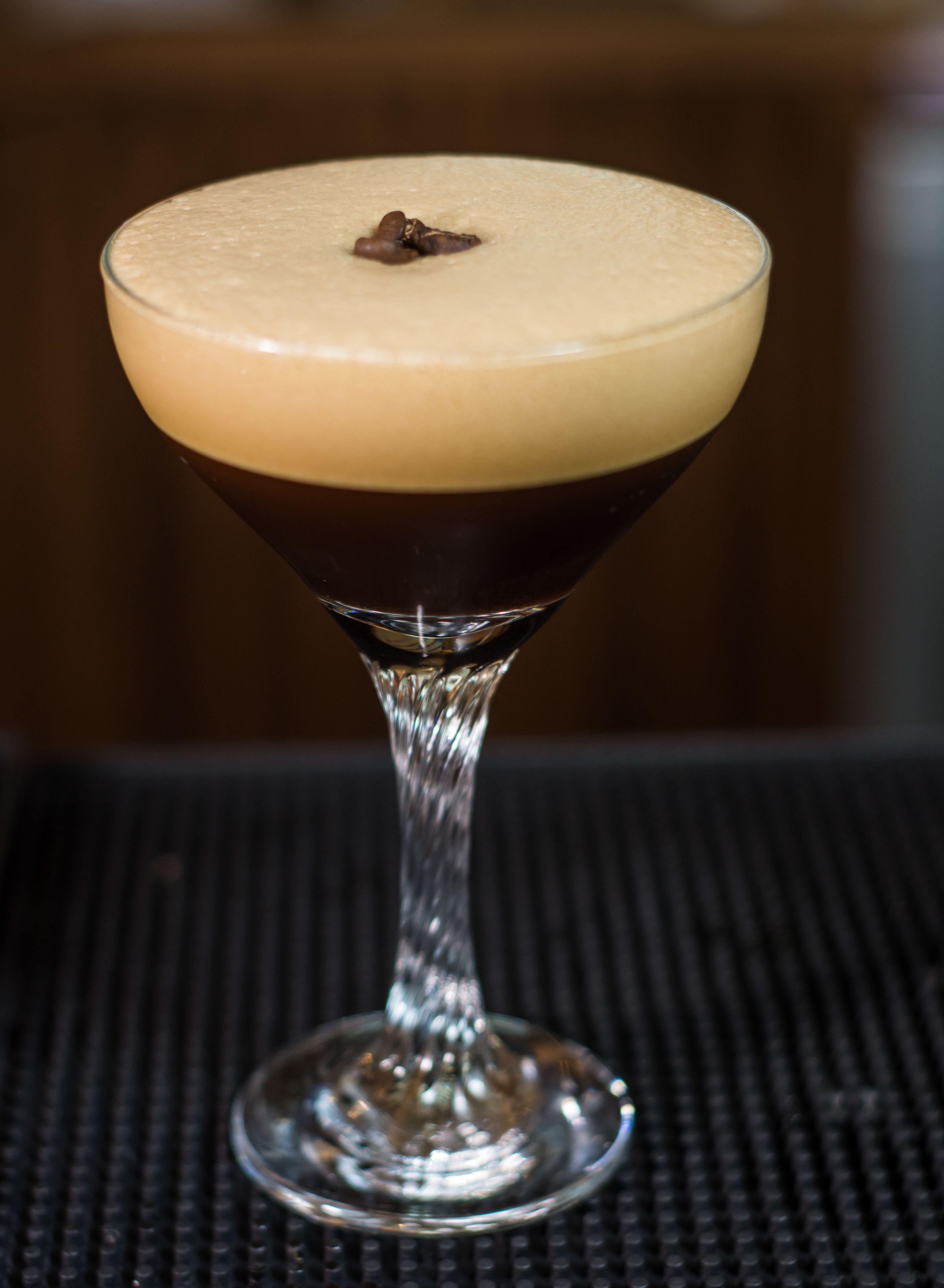 A martini glass with a layered drink on a textured surface.