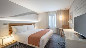Una habitación de hotel con cama, mesita de noche, lámpara, televisor y una pared con una cita.