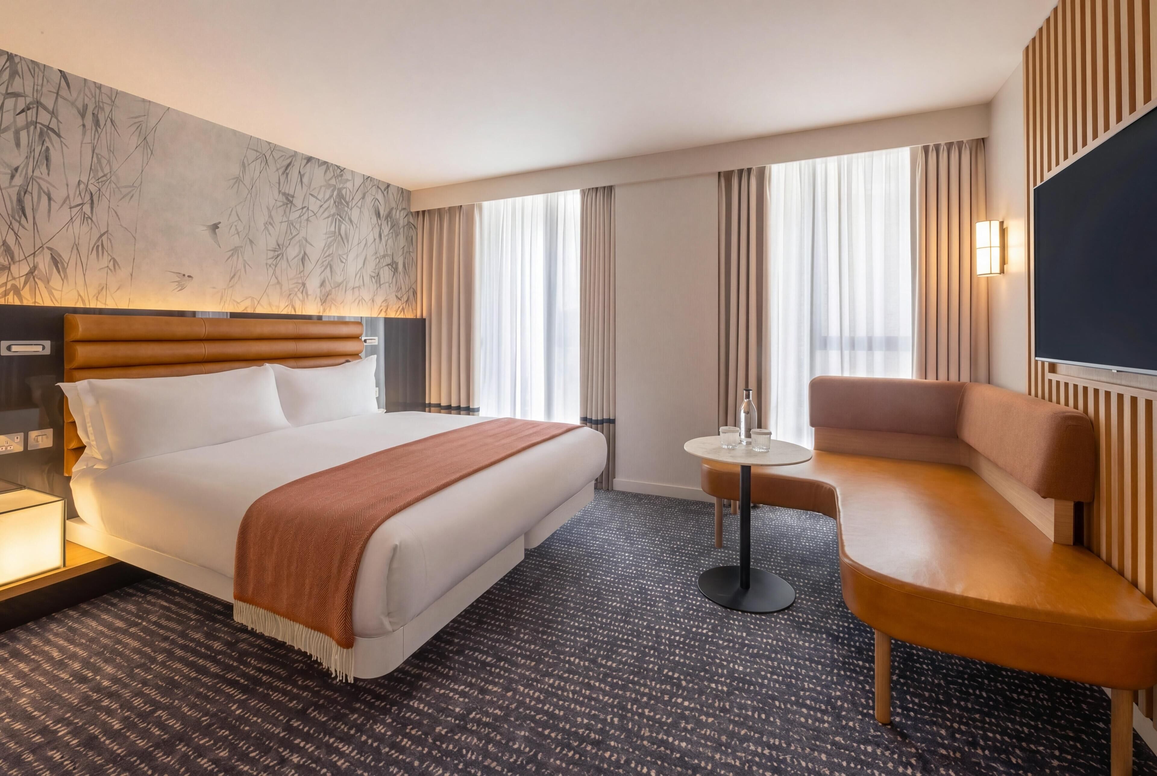 Habitación de hotel con una cama grande, un sofá, una mesita, un televisor y una pared con estampado de bambú.