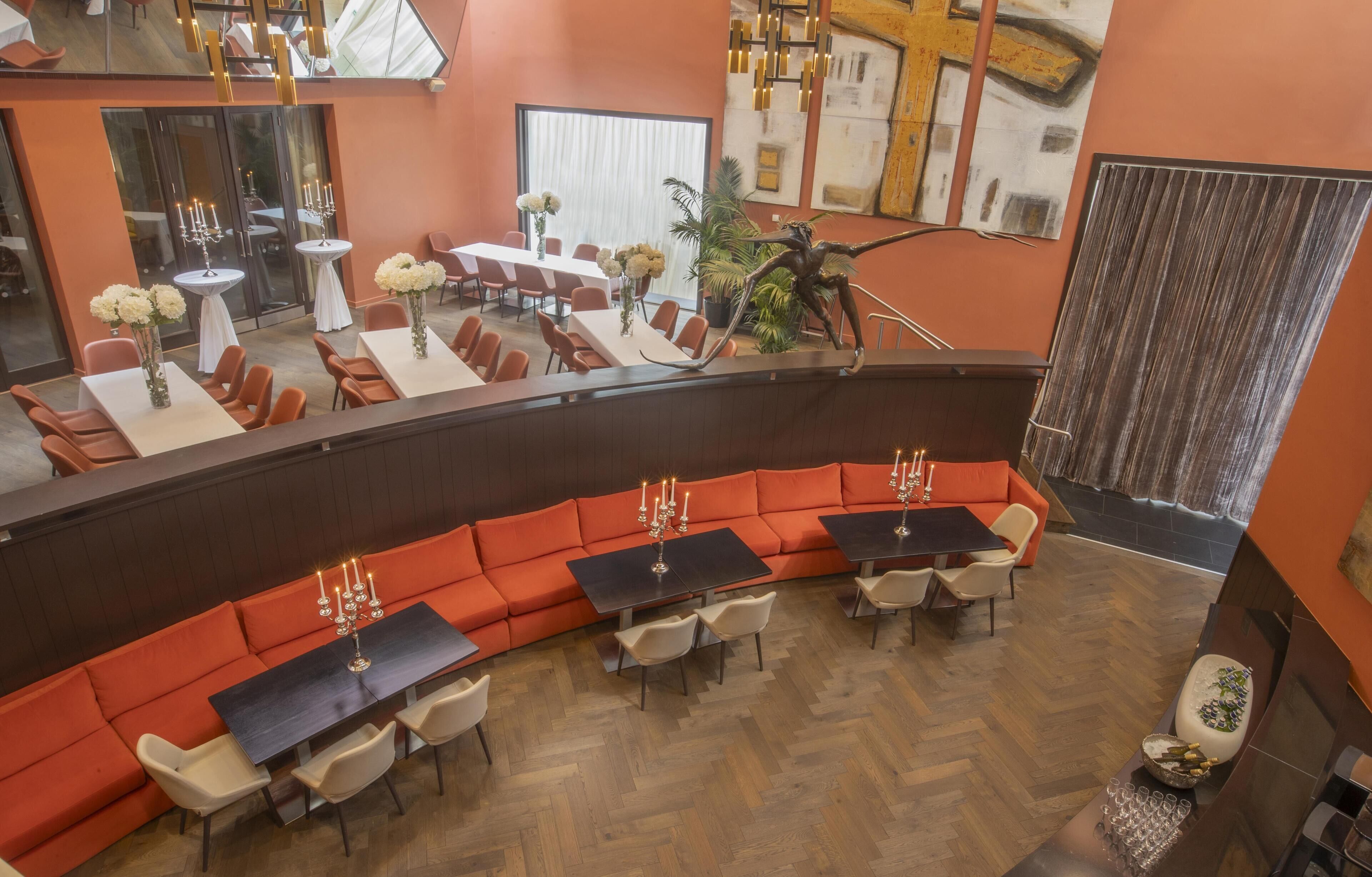 Una hall d'albergo moderna con un'area salotto dalle linee curve, diversi tavoli e una scala.