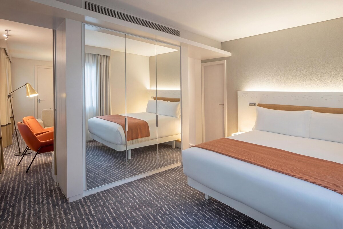 Ein Hotelzimmer mit einem großen Bett, einem Sessel, einem Schreibtisch und einem Spiegel.