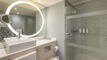 A modern bathroom with a round mirror, a sink, a toilet, and a shower area.