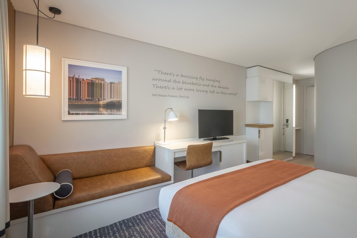 Ein Hotelzimmer mit Bett, einer Couch, einem Schreibtisch mit Fernseher, einer Lampe und einer Wand mit einem Zitat.