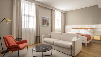 A hotel room with a bed, a sofa, a chair, a small table, and a lamp.