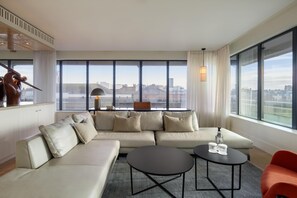 Una sala de estar moderna con un sofá grande, una mesa de centro y vistas de la ciudad a través de amplias ventanas.