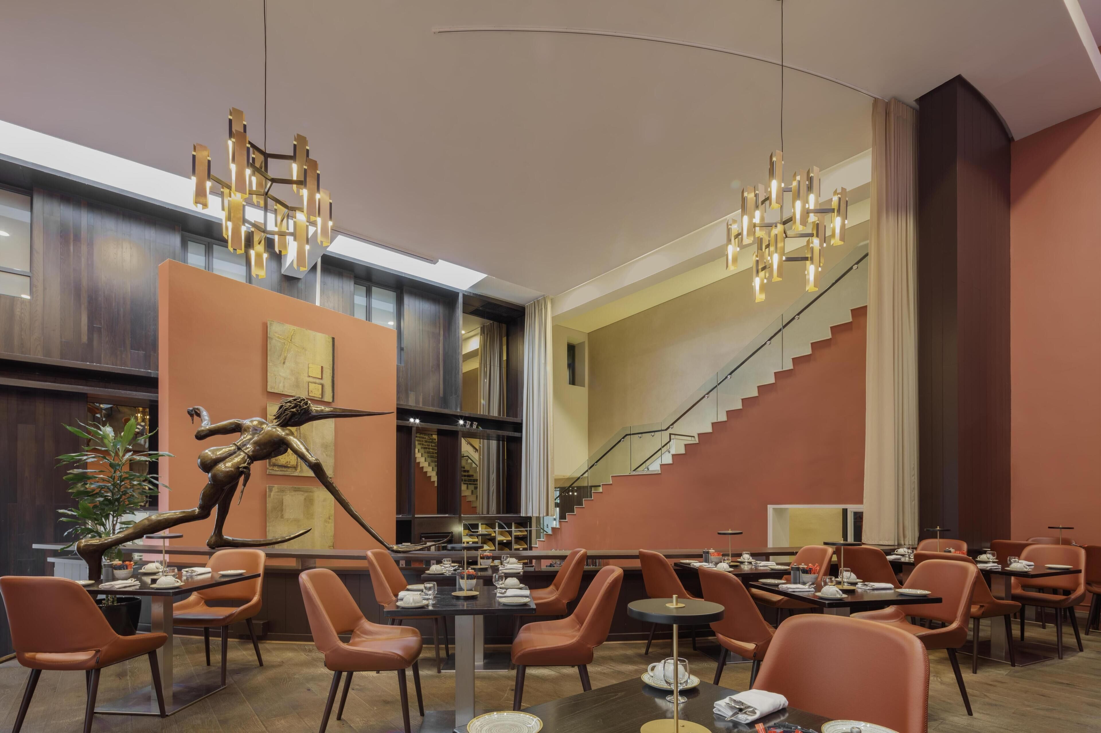 A modern dining area with a central sculpture, a staircase, and a view of the kitchen.