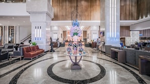 A spacious lobby with a central round table surrounded by sofas, a reception desk, and a staircase in the background. - Arnoma Grand (Bangkok)