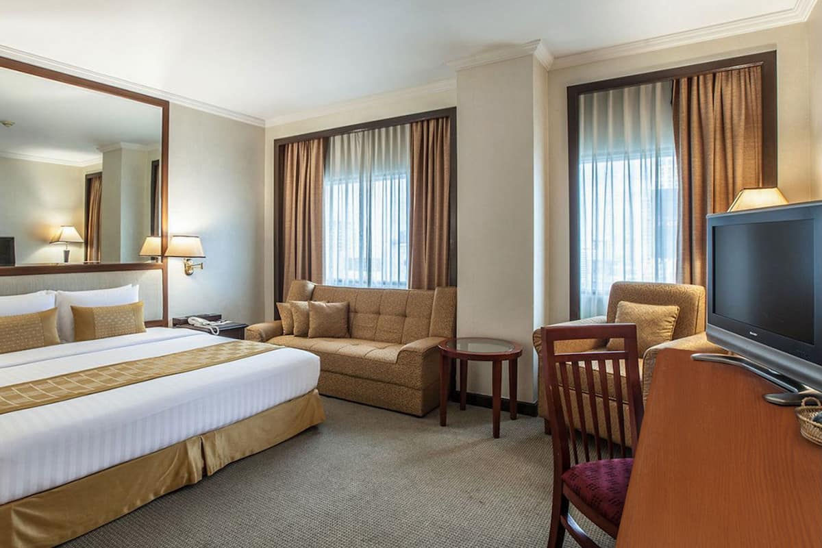 A hotel room with a large bed, a sofa, a chair, a desk, and a TV.