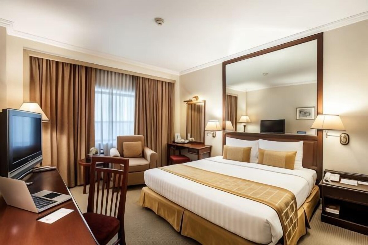 Una habitación de hotel con una cama grande, un escritorio con una computadora portátil, un televisor y una silla.