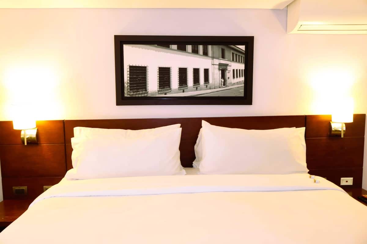 A hotel room with a large bed, two bedside lamps, a framed picture on the wall, and a nightstand with a lamp.