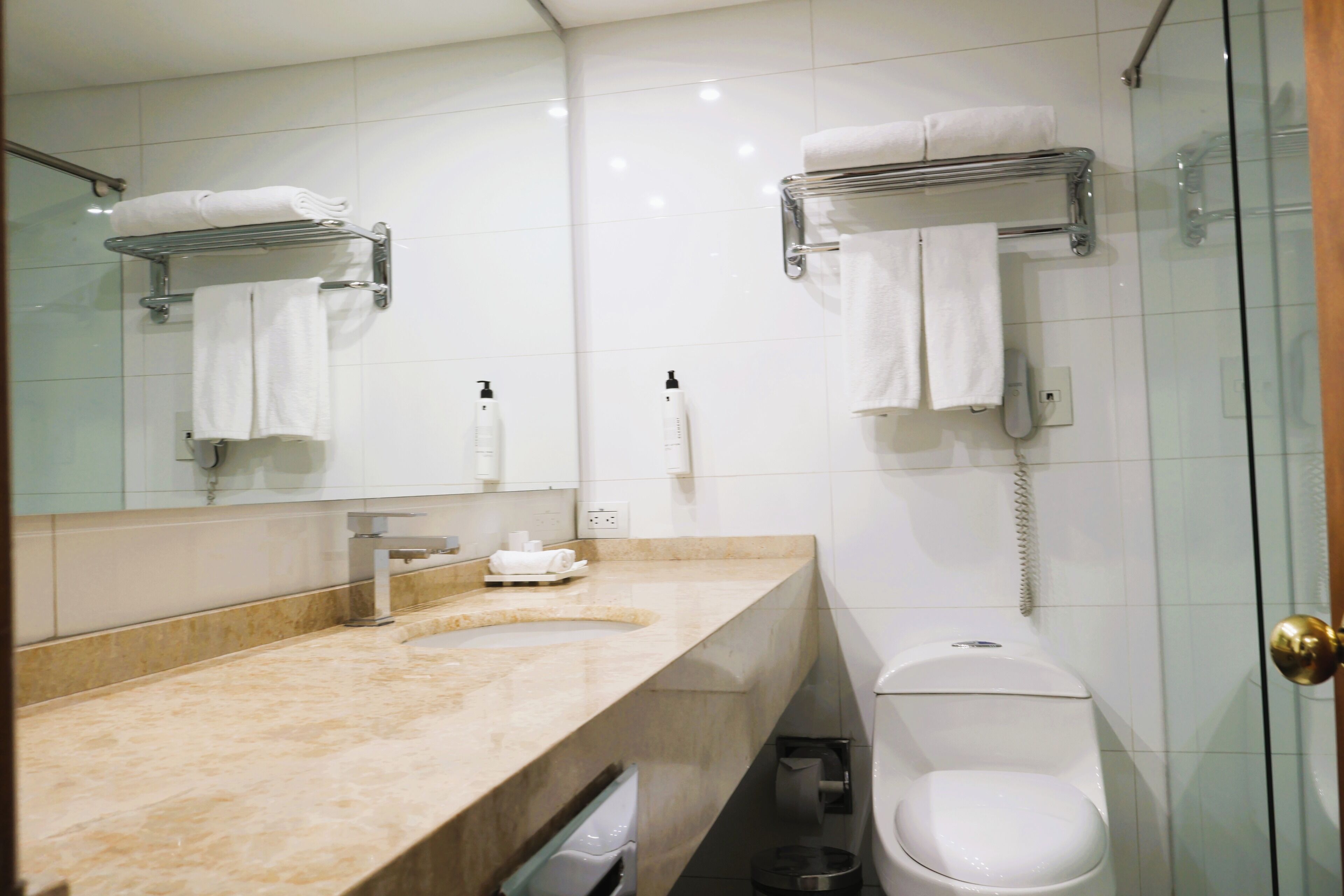 A modern bathroom with a marble sink, a toilet, a glass shower enclosure, and a towel rack.