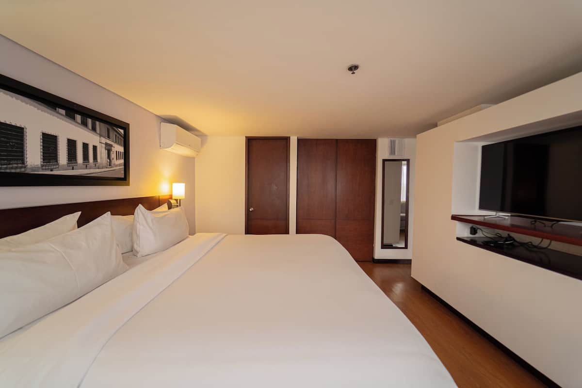 A hotel room with a large bed, a television, a wardrobe, and a framed picture on the wall.