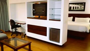 A hotel room with a bed, a desk with a computer, a glass coffee table, and a chair.