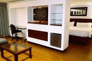 A hotel room with a bed, a desk with a computer, a glass coffee table, and a chair.