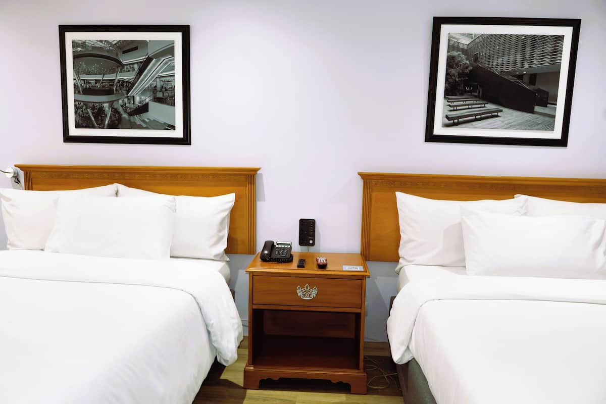 A hotel room with two beds, a nightstand with a phone, and two framed pictures on the wall.