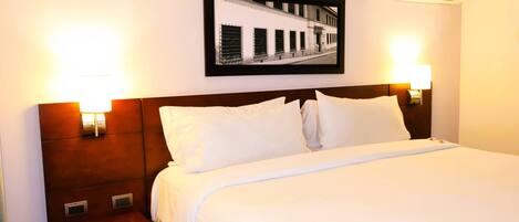A hotel room with a large bed, two bedside tables, a framed picture on the wall, and two wall-mounted lamps.