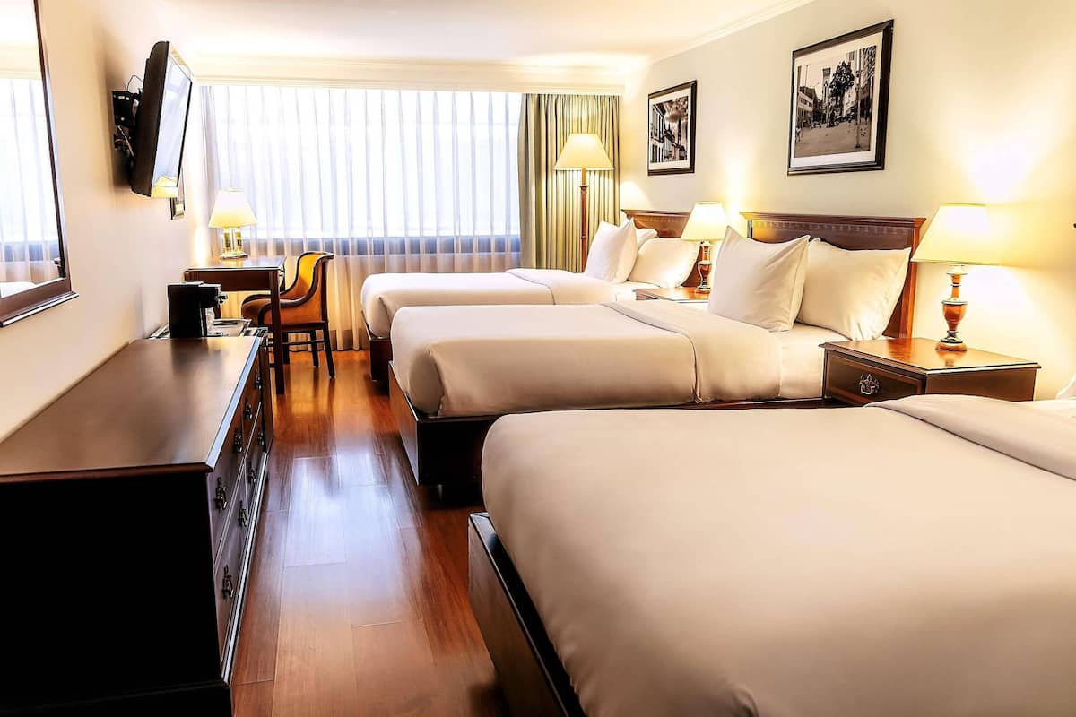 A hotel room with two beds, a desk, a chair, a TV, and a window with curtains.