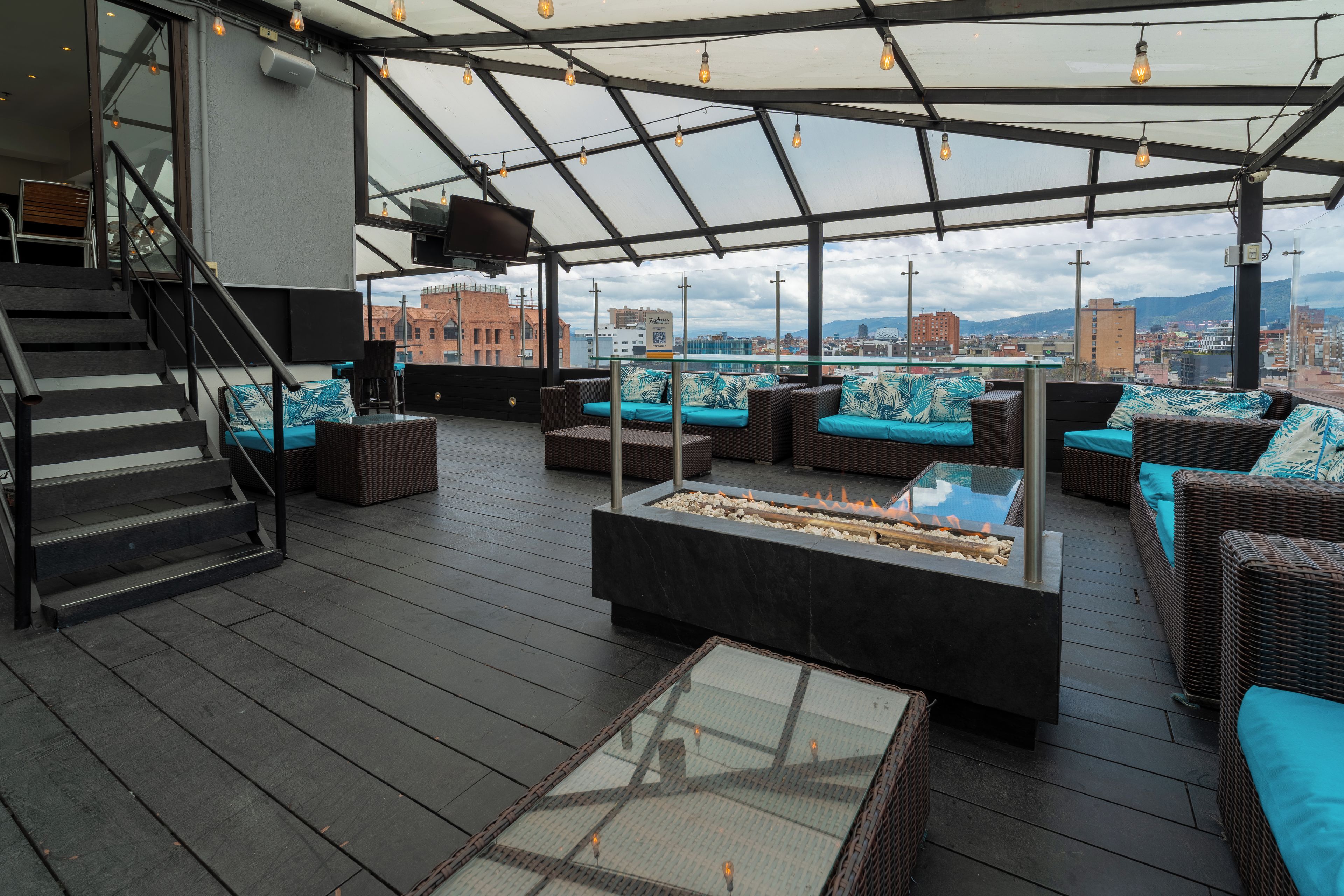 A rooftop terrace with wicker furniture, a glass-top table, and a fire feature.