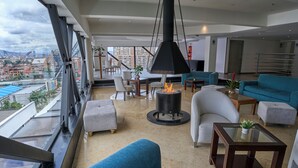 A modern living room with a large window, a hanging fire pit, and a city view. - Radisson Bogota Metrotel (Bogotá)