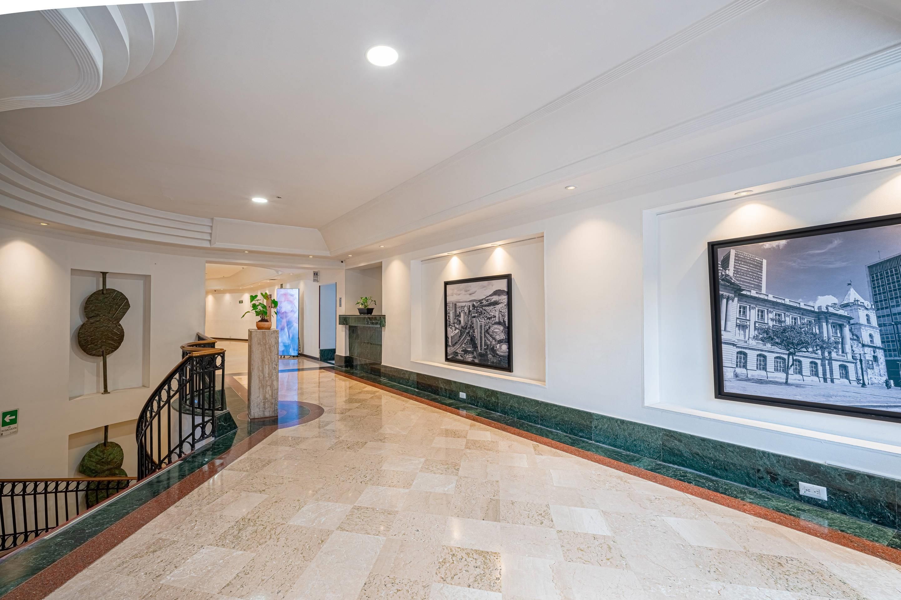 Un pasillo de hotel con piso de mármol, una escalera y cuadros enmarcados en las paredes.