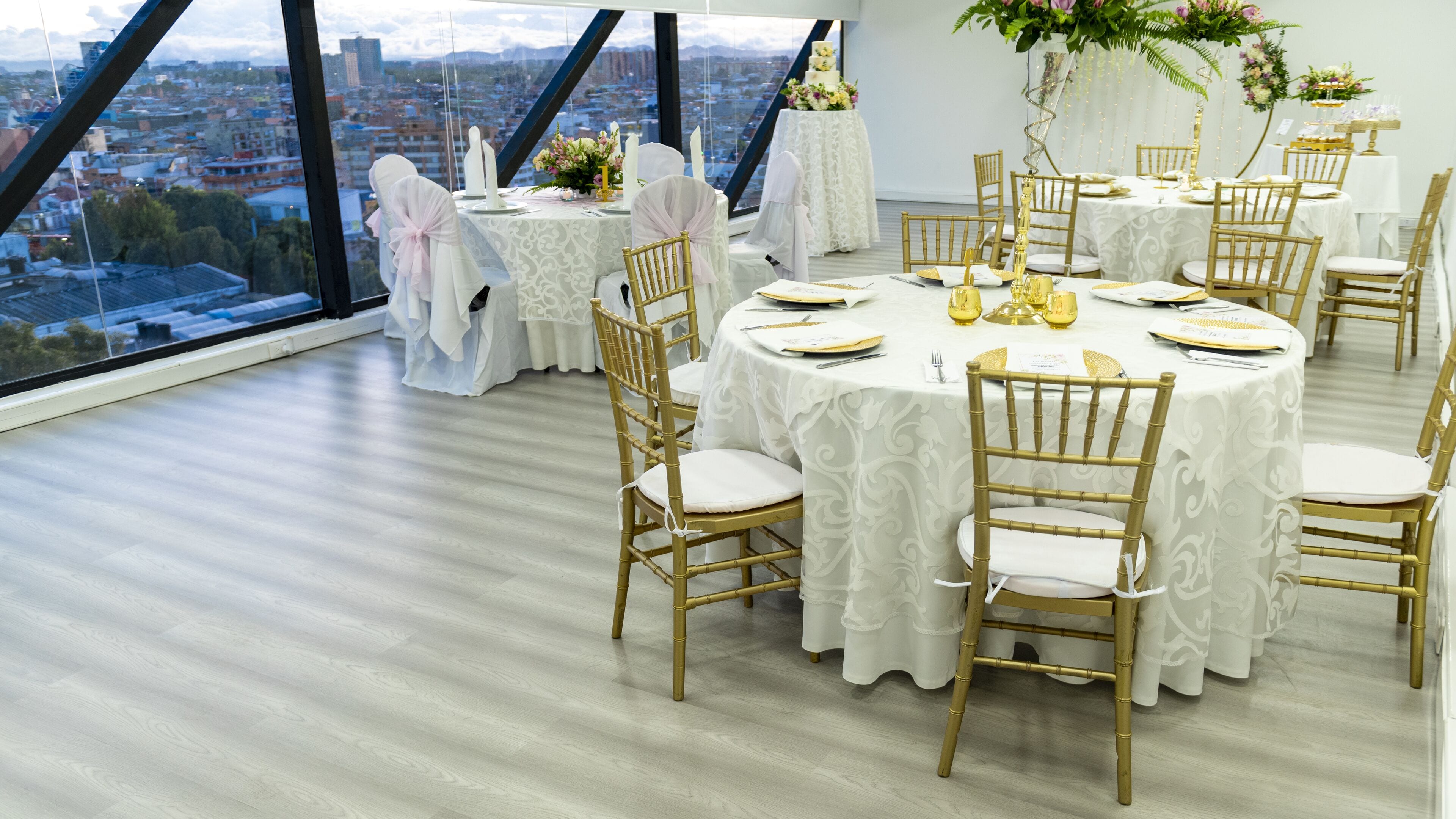 A round table with gold chairs and white tablecloths, set against a city view.