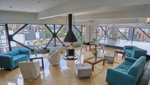 A spacious lounge with teal sofas, a central fire feature, and large windows offering city views. - Radisson Bogota Metrotel (Bogotá)