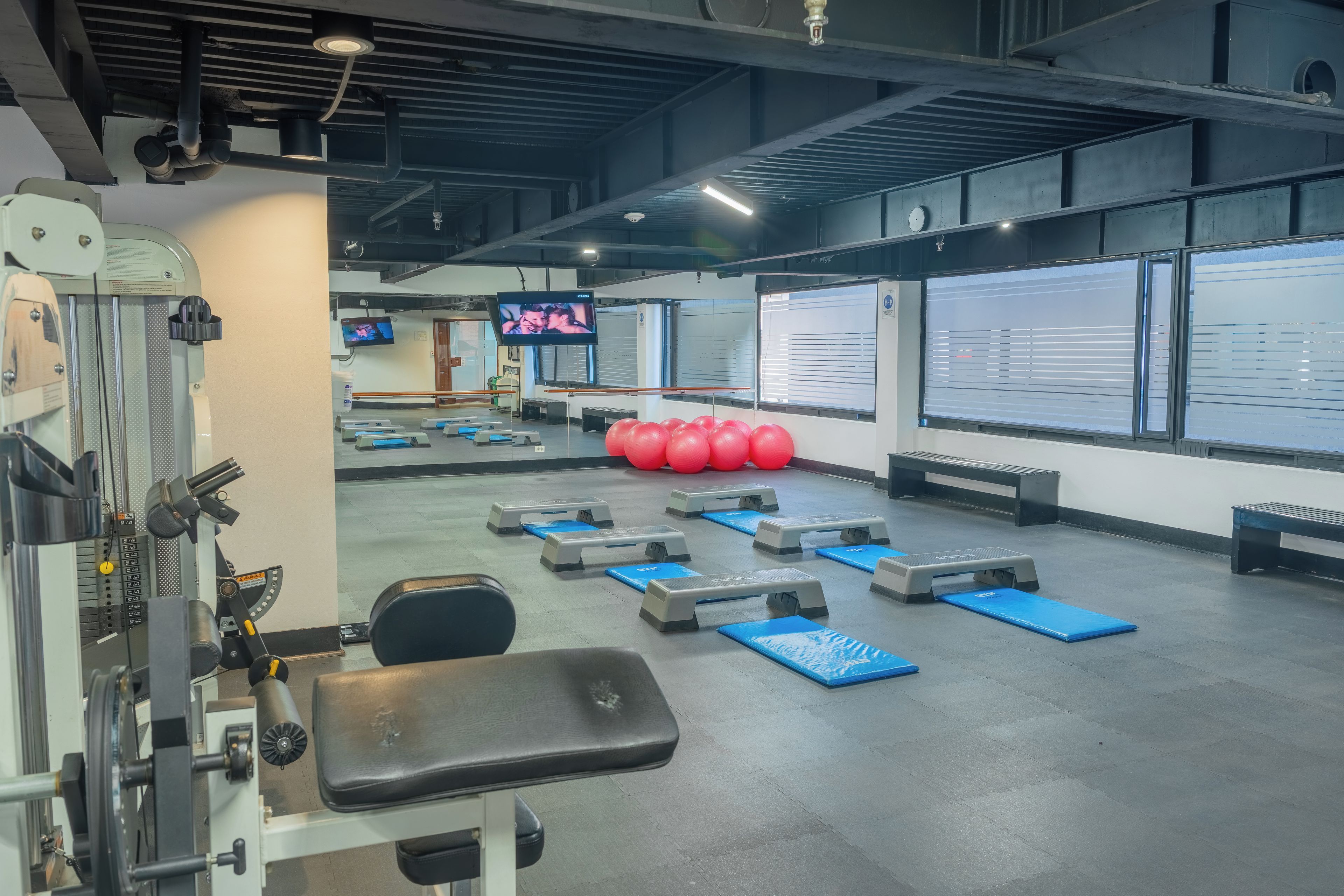 Un gimnasio con equipo de ejercicio, cintas de correr y balones de ejercicio rojos.