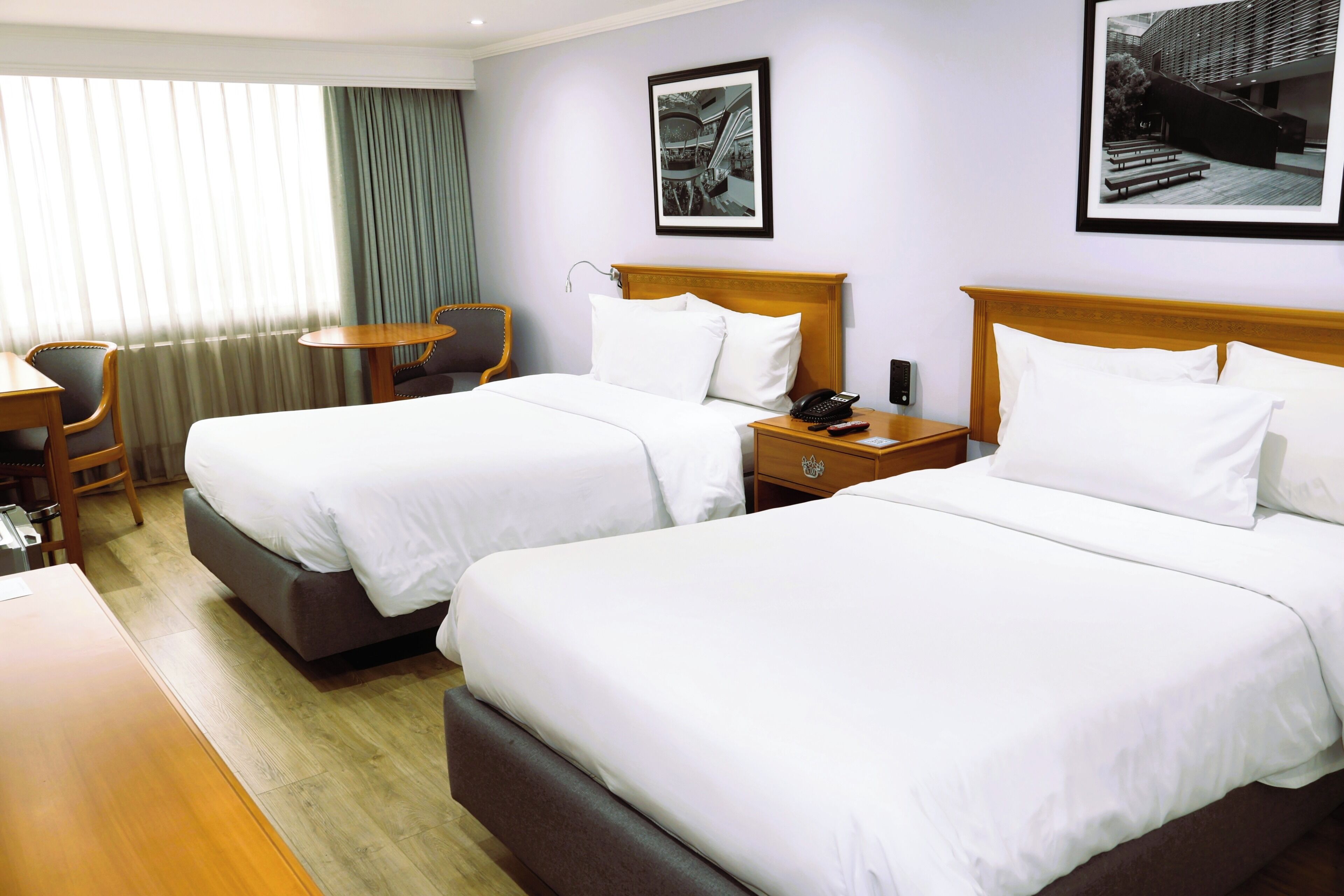 Habitación de hotel con dos camas, un escritorio, una silla y una ventana con cortinas.