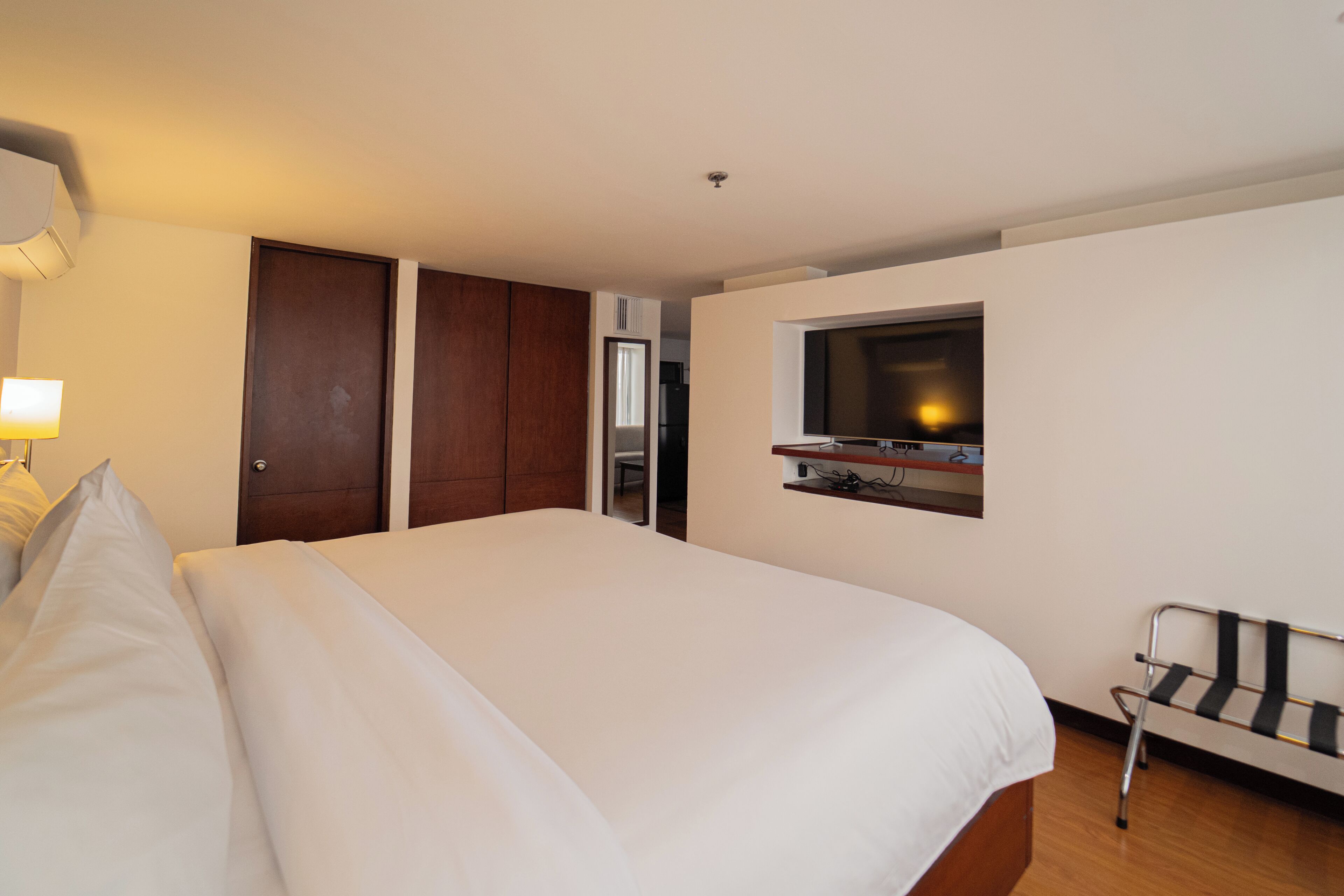Habitación de hotel con una cama grande, un televisor montado en la pared, una silla y un escritorio con una computadora.