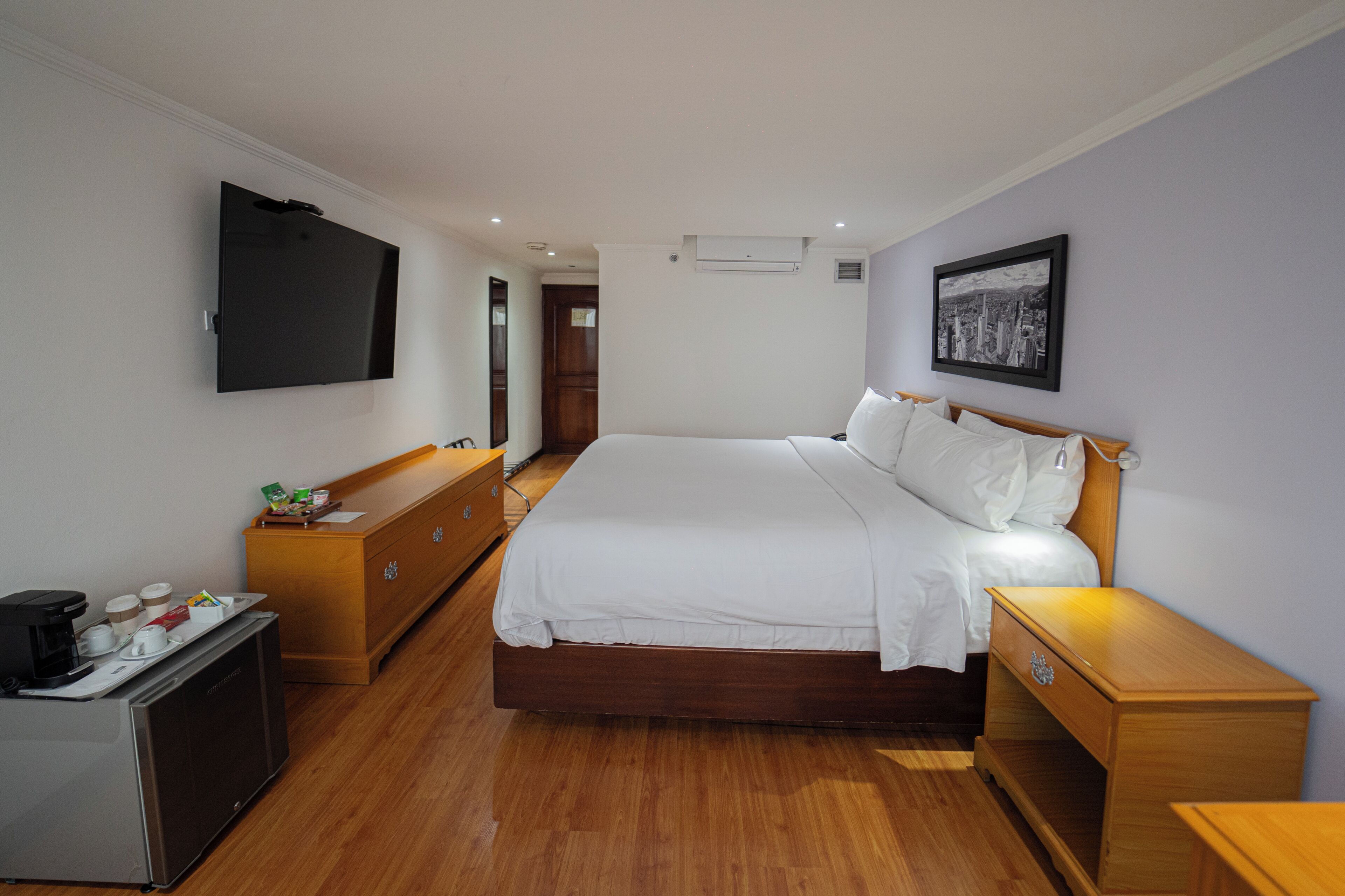 Habitación de hotel con cama, mesita de noche, cómoda y televisor montado en la pared.