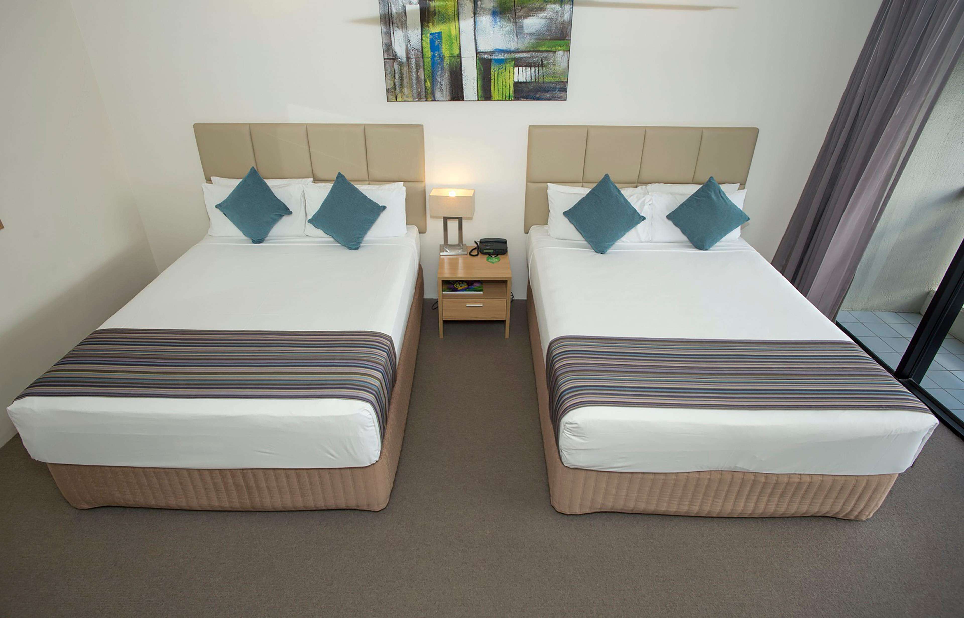 A hotel room with two beds, each with a headboard, a nightstand, and a lamp.