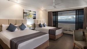 Habitación de hotel con dos camas, un ventanal con vistas, un ventilador de techo y un cuadro en la pared.
