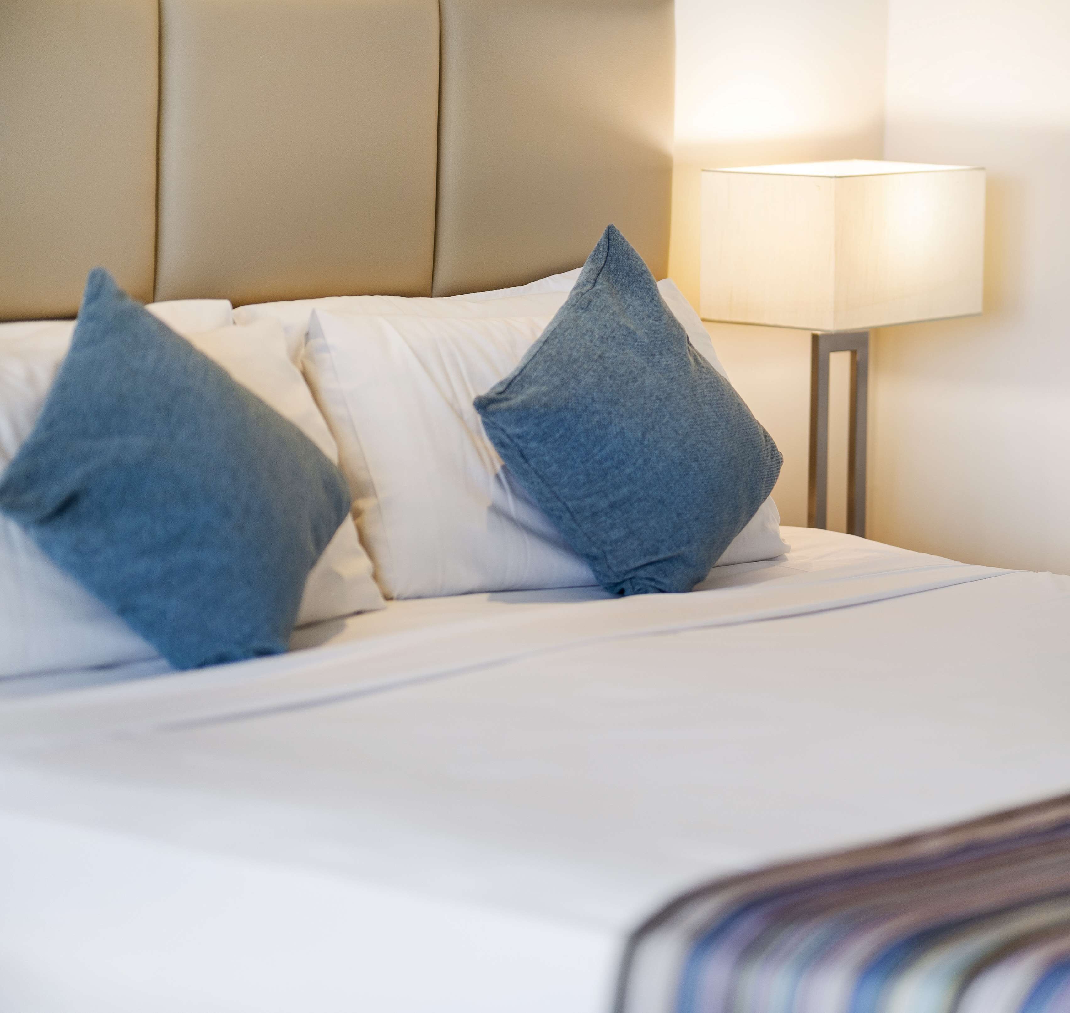 A neatly made bed with white linens and two blue pillows.