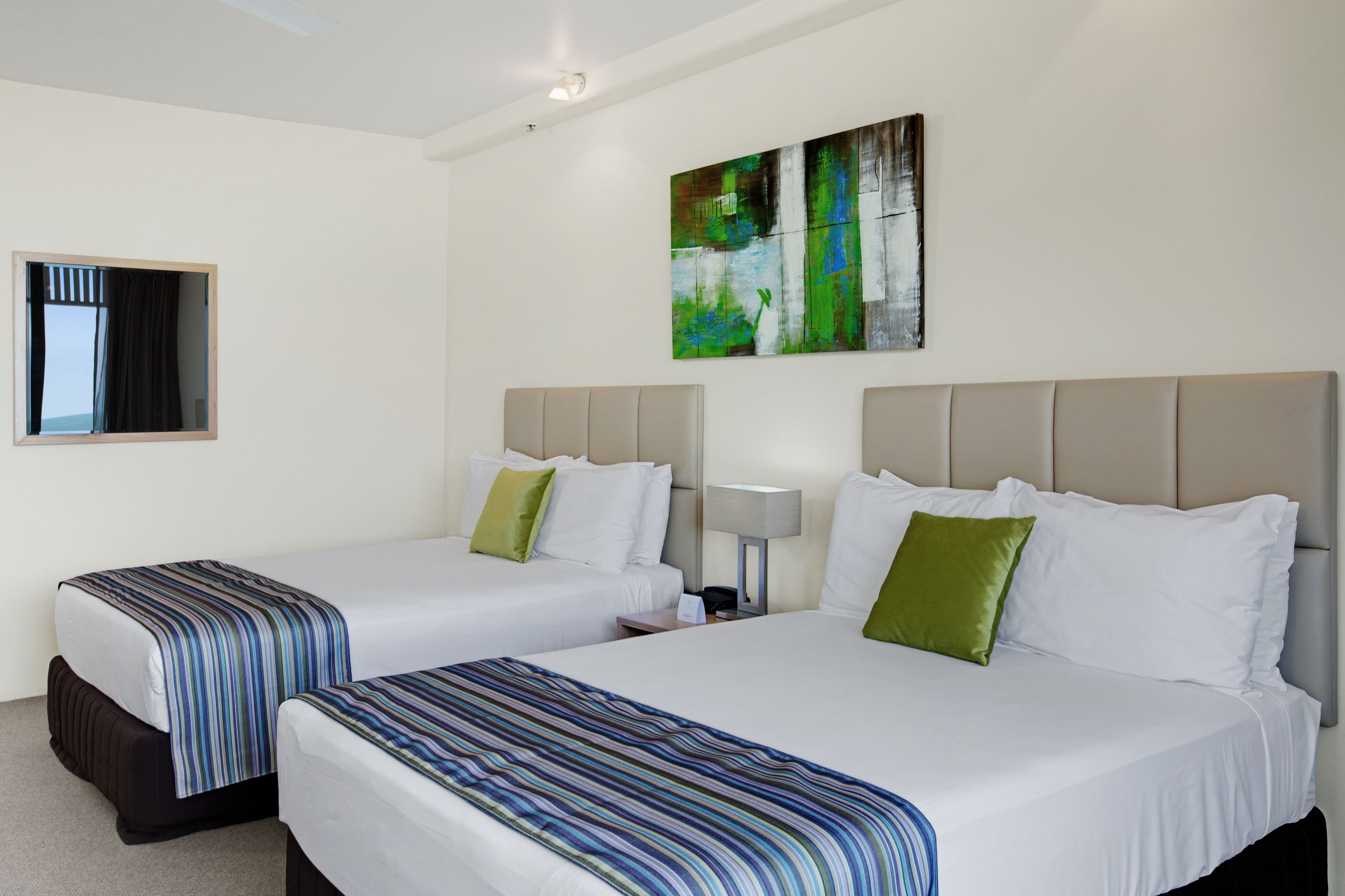 Una camera d'albergo con due letti, un grande quadro astratto appeso al muro, una finestra con vista e un comodino con una lampada.