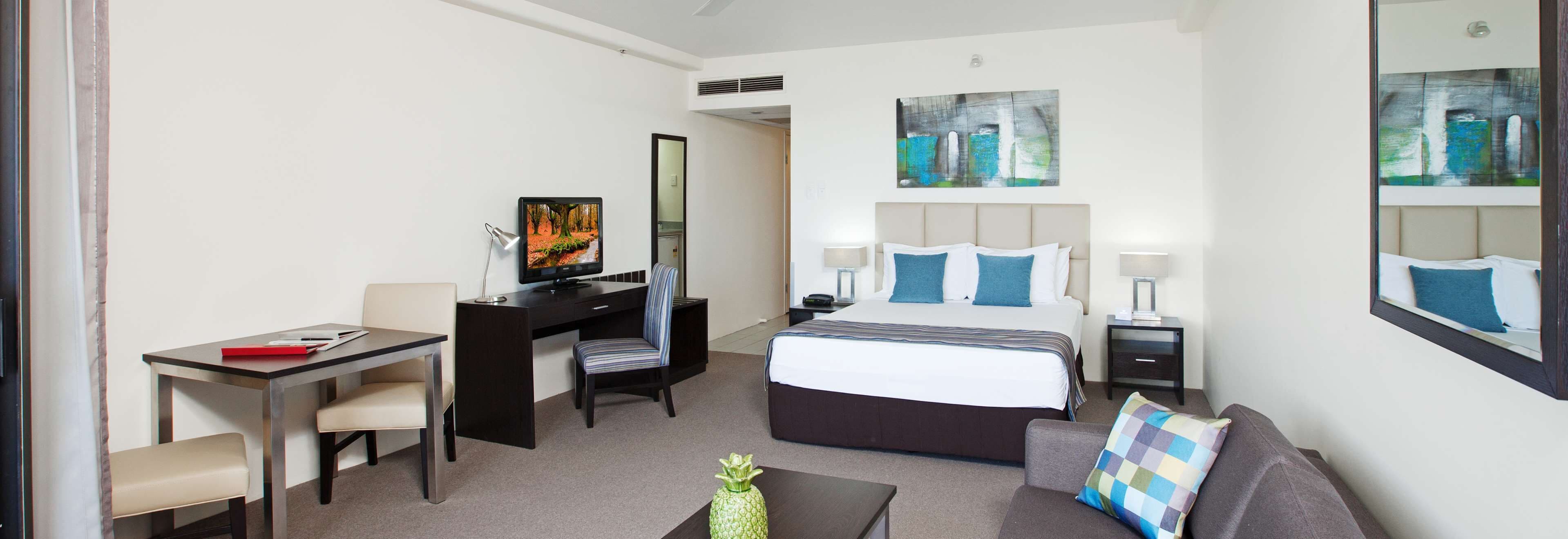 A hotel room with a bed, a desk, a chair, a sofa, and artwork on the walls.