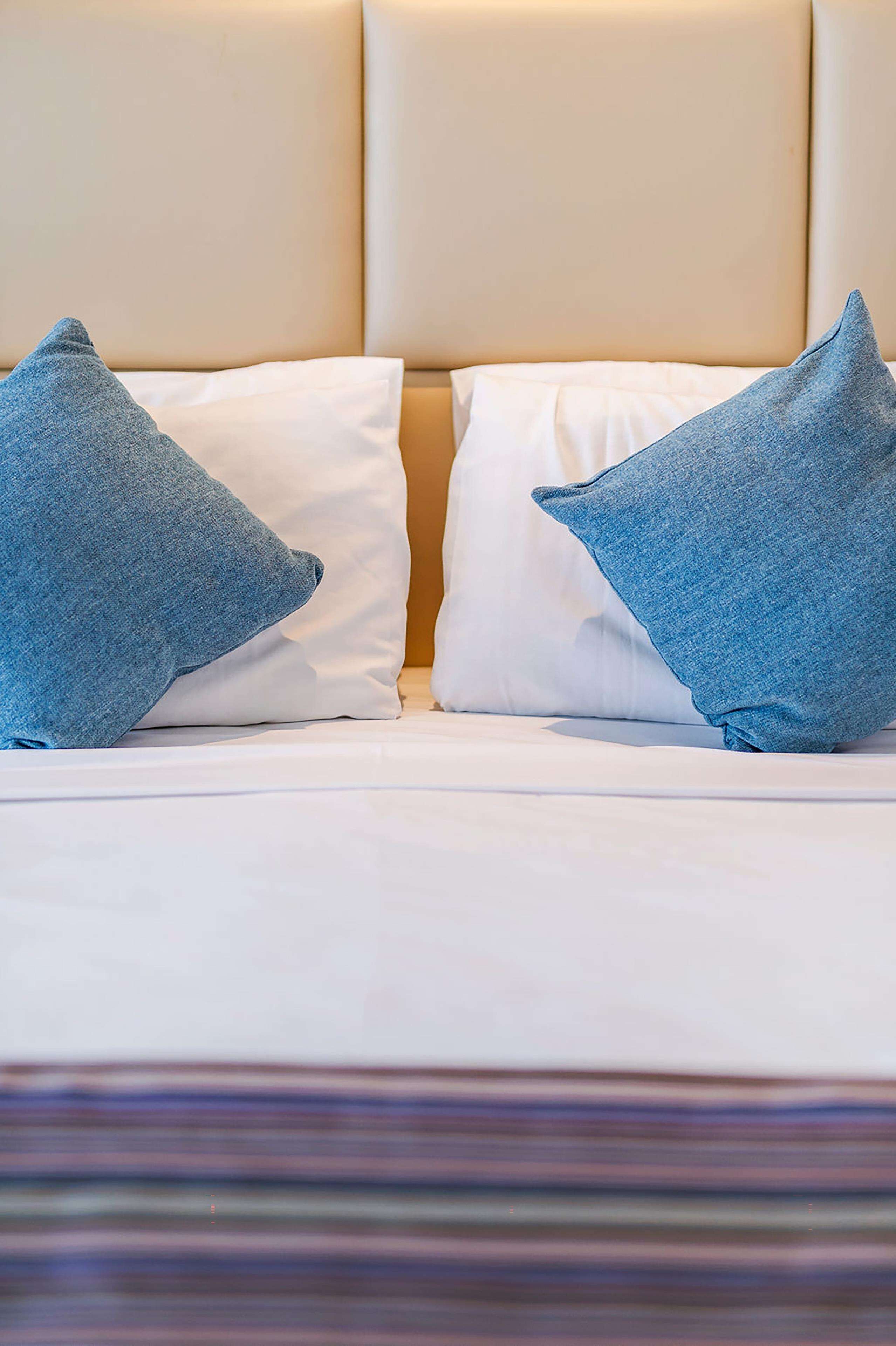A bed with white linens and two blue pillows.
