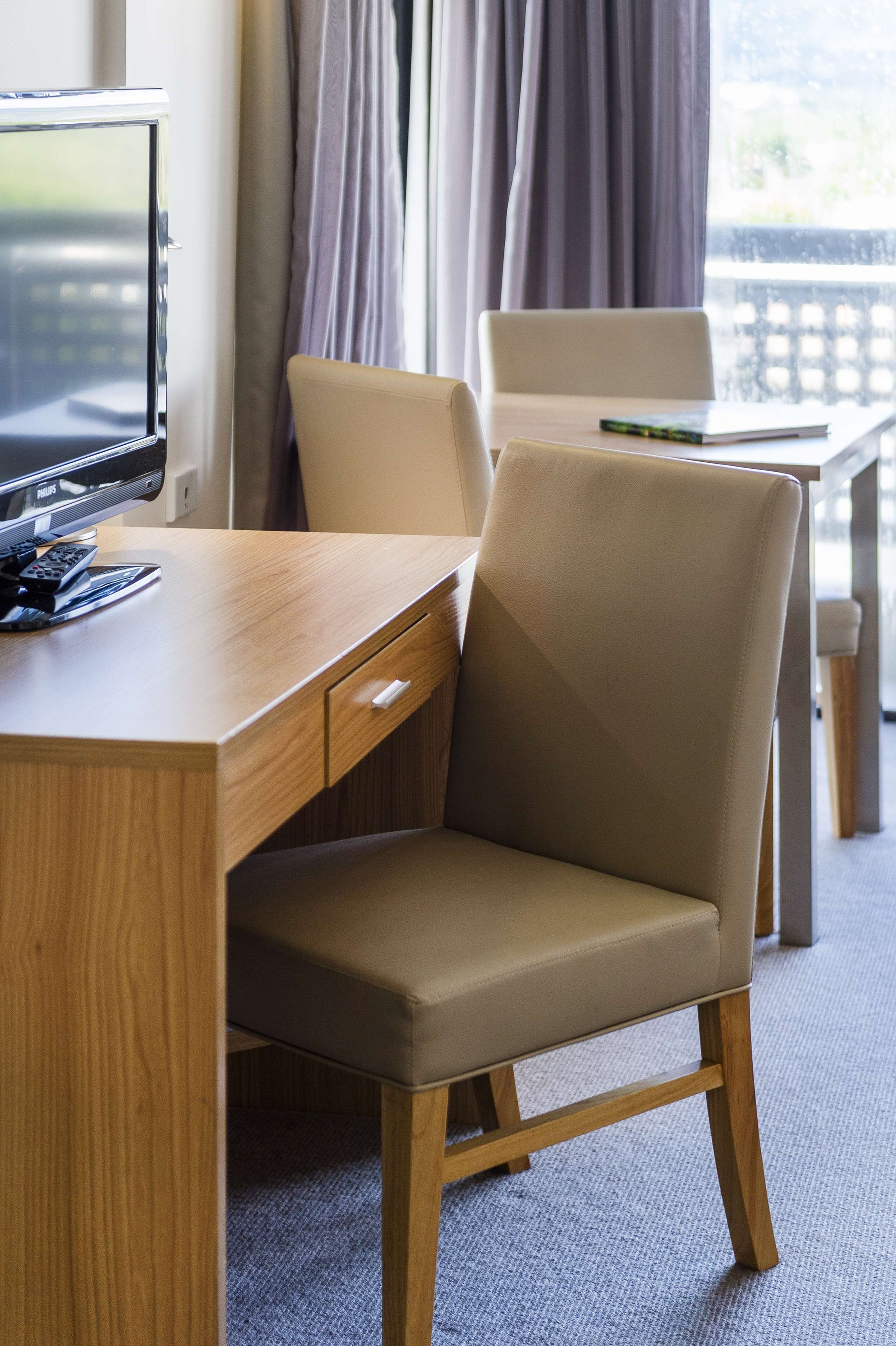 Une chambre d’hôtel avec un bureau en bois, une chaise beige et un téléviseur.