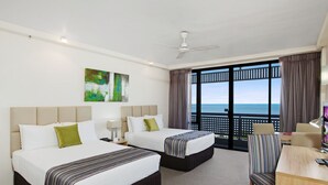 Habitación de hotel con dos camas, un escritorio, una silla y un ventanal con vista al mar.