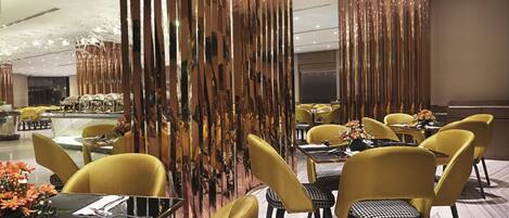 Un área de comedor moderna con sillas amarillas, mesas negras y paneles verticales decorativos.