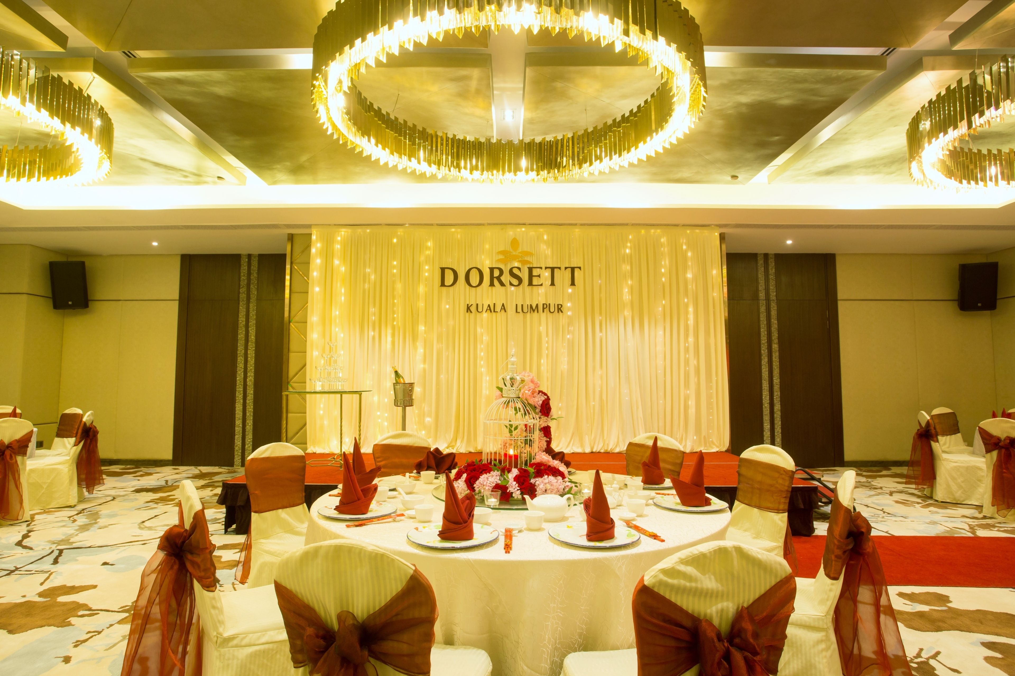 A banquet hall with round tables set for a formal event, featuring a central floral arrangement and a backdrop with the name 'DORSETT KUALA LUMPUR'.