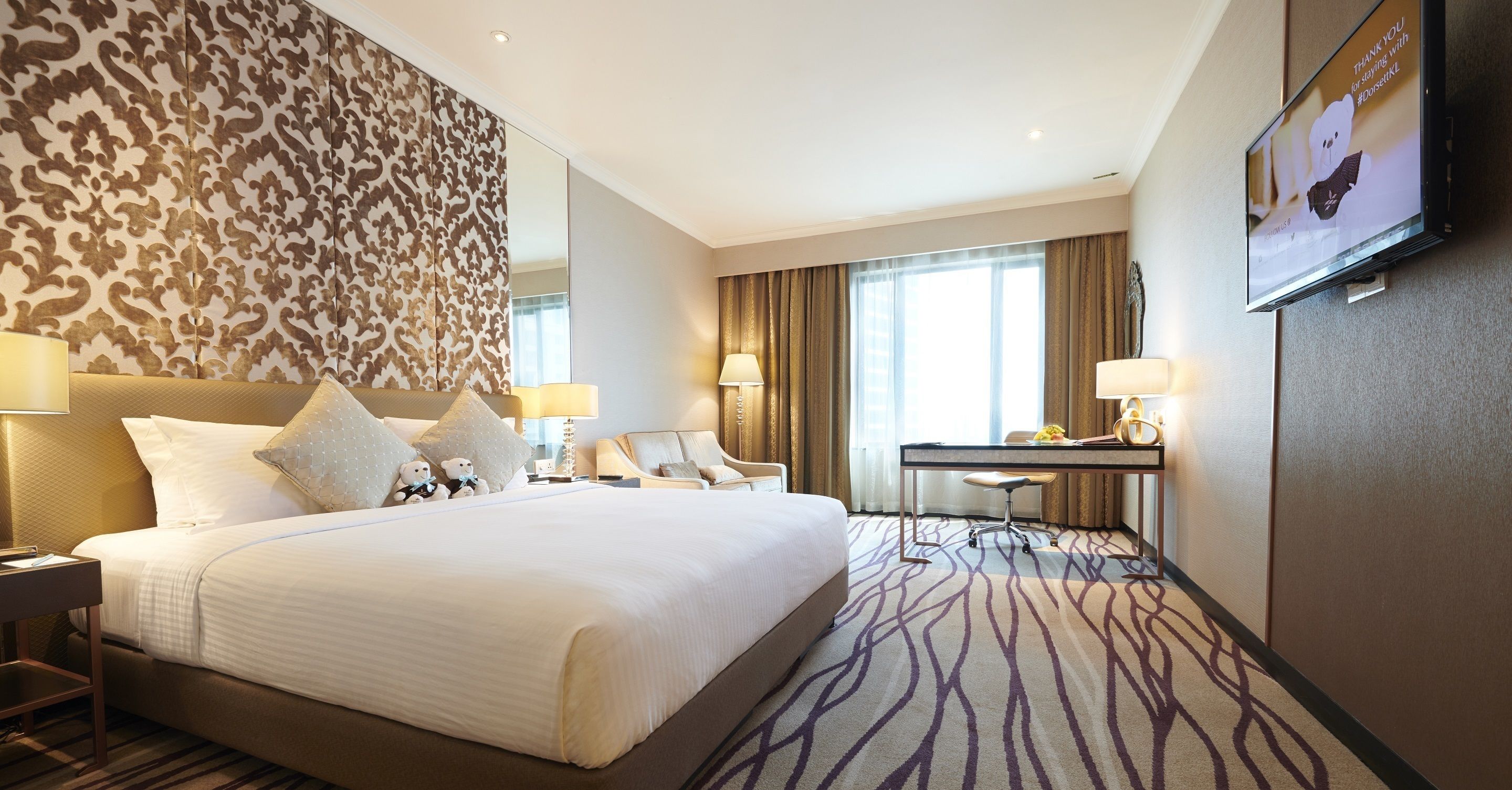 A hotel room with a large bed, a desk, a chair, and a TV on the wall.