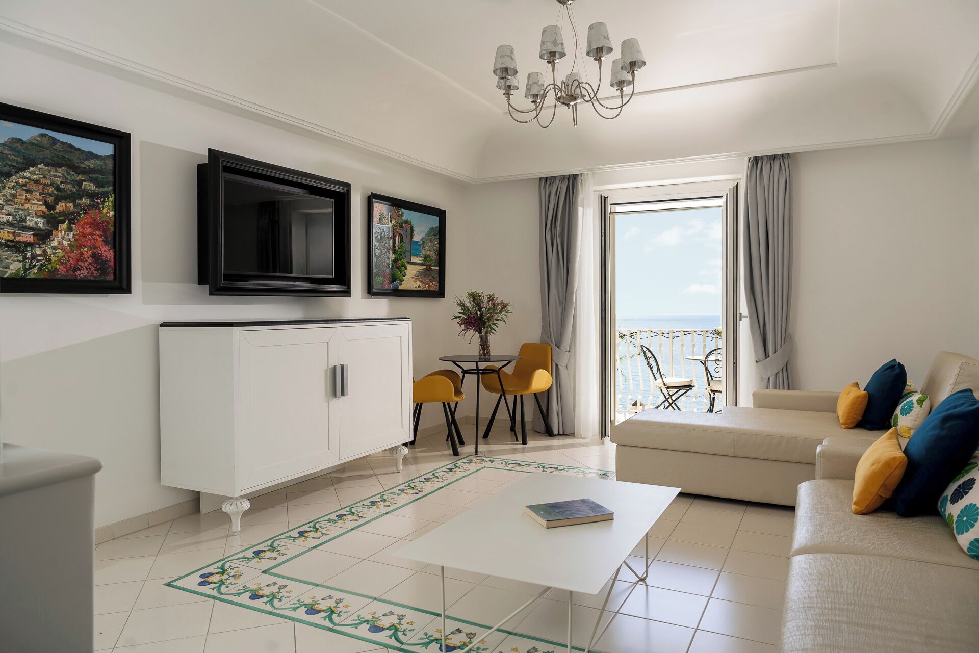 Una sala de estar con sofá, una mesa de centro, una mesa de comedor con sillas, un televisor y un balcón con vistas al mar.
