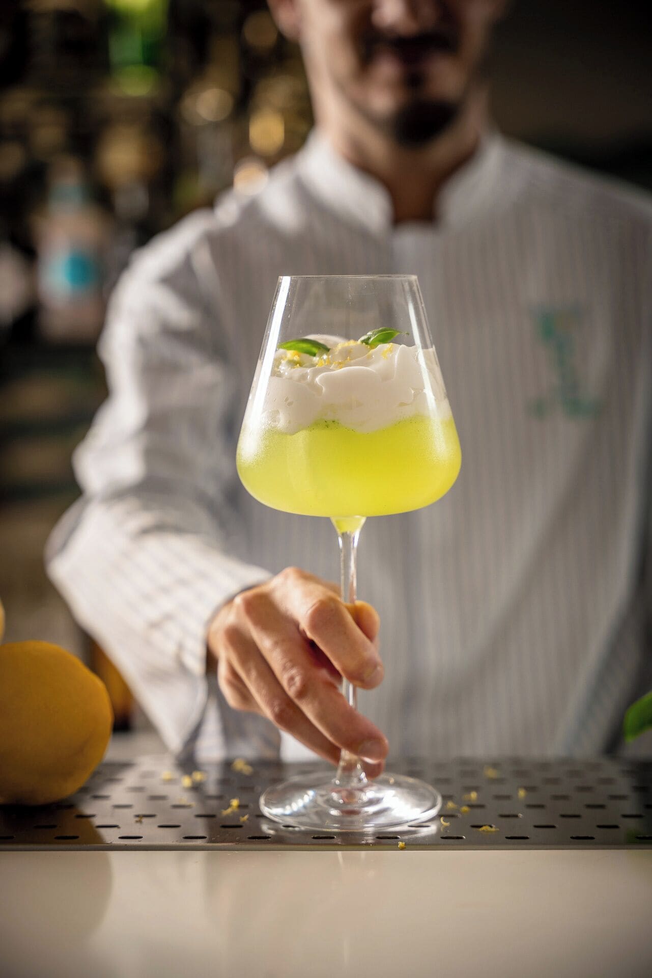 Una persona sosteniendo una copa de cóctel con líquido amarillo y crema batida.