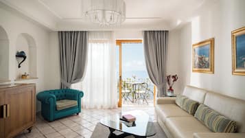 A living room with a teal sofa, a beige sofa, a glass coffee table, and a view of the sea through a balcony door.