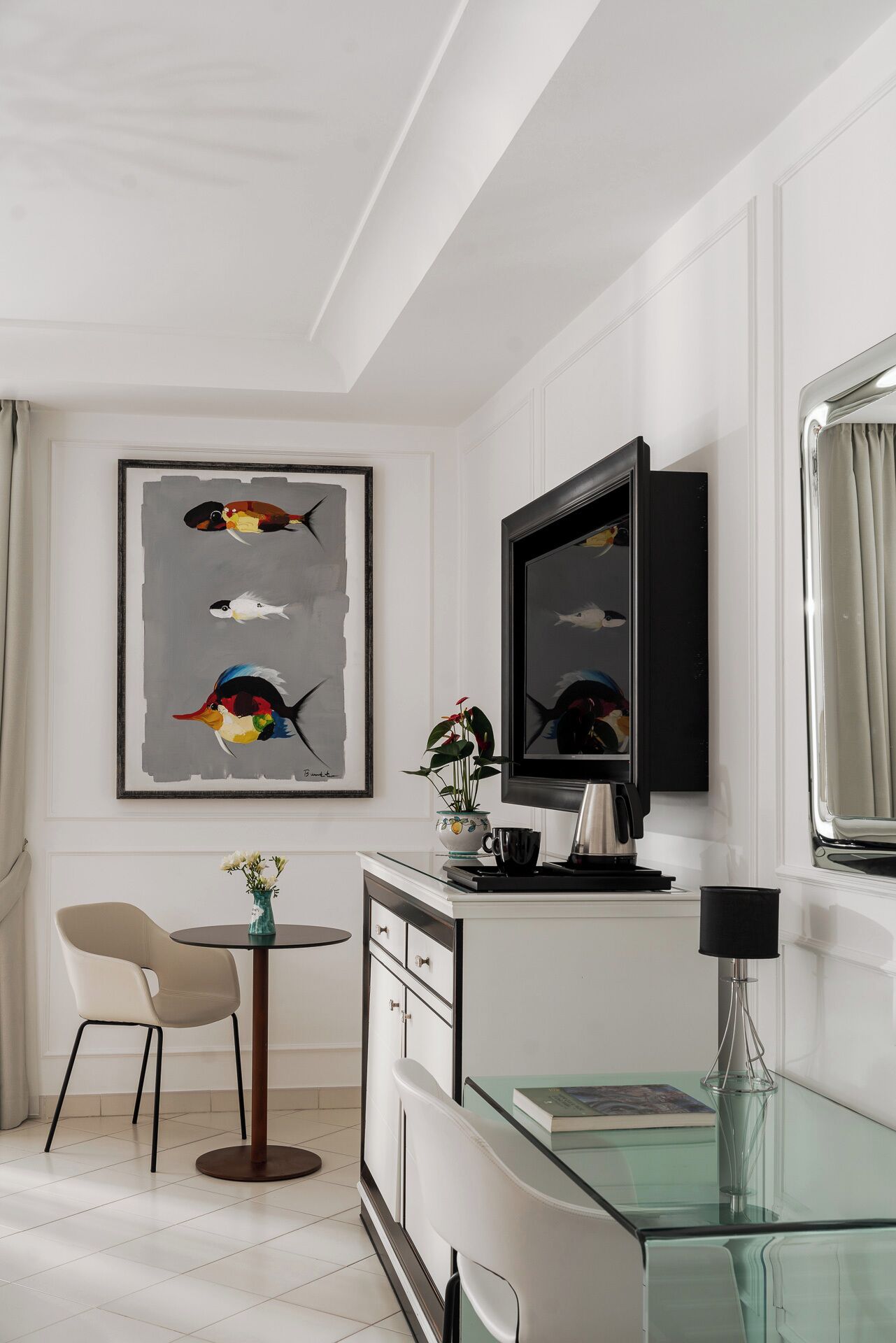 A modern living room with a flat-screen TV, a glass coffee table, a beige chair, and a framed abstract painting.