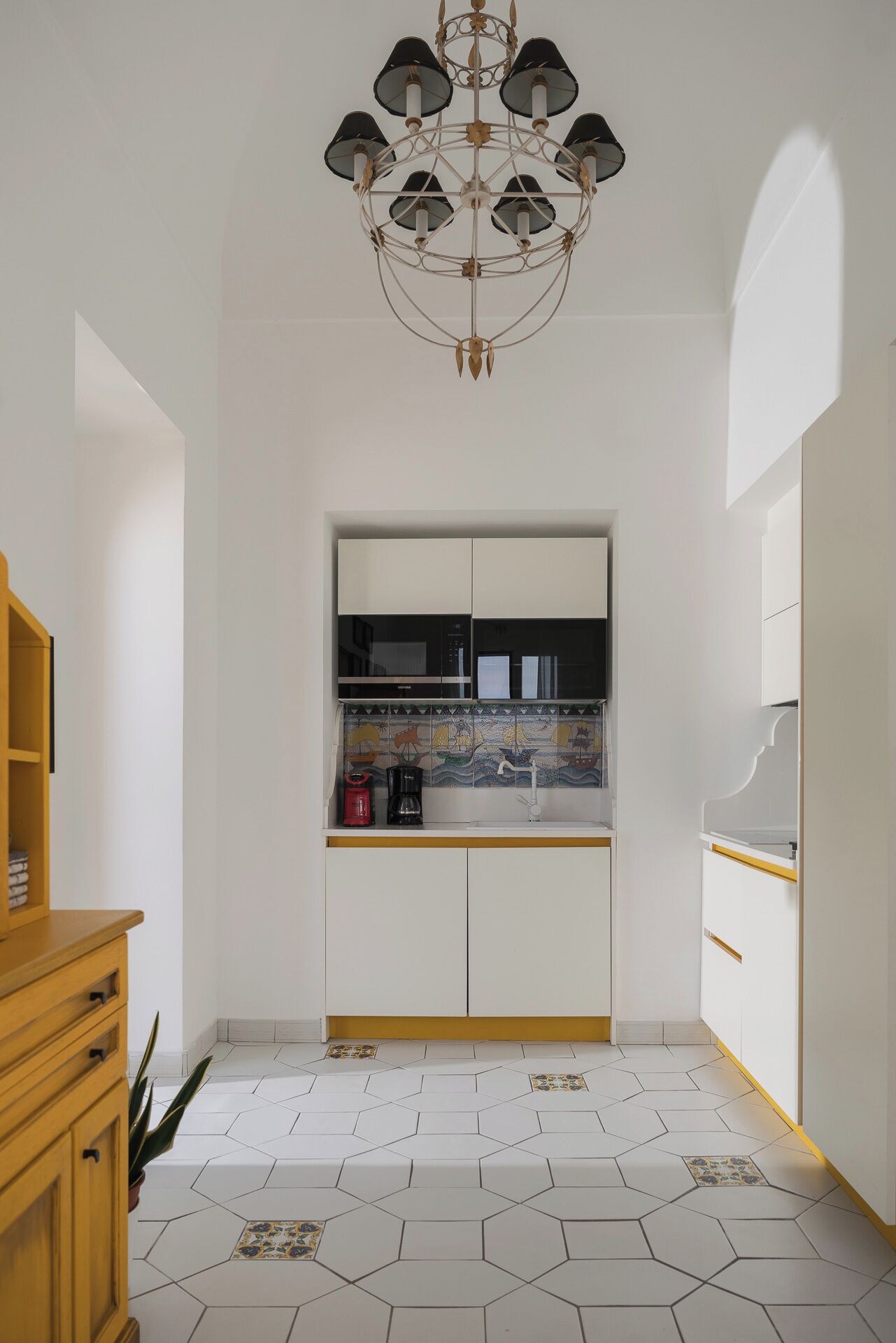 Una cocina moderna con armarios blancos, suelo de baldosas hexagonales y una lámpara colgante original.