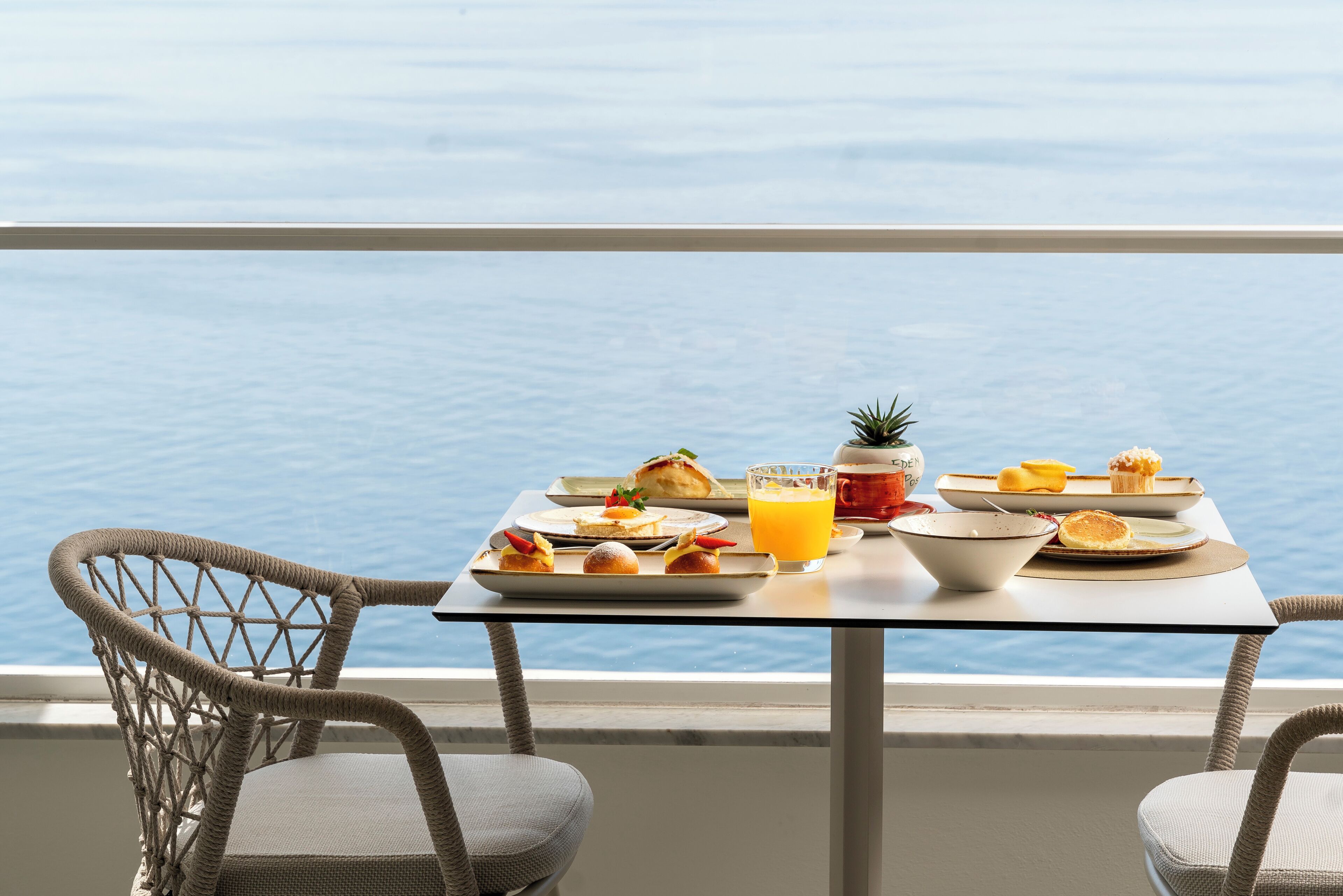 Un tavolo con cibi per la colazione e un bicchiere di succo d'arancia su un balcone affacciato sul mare.