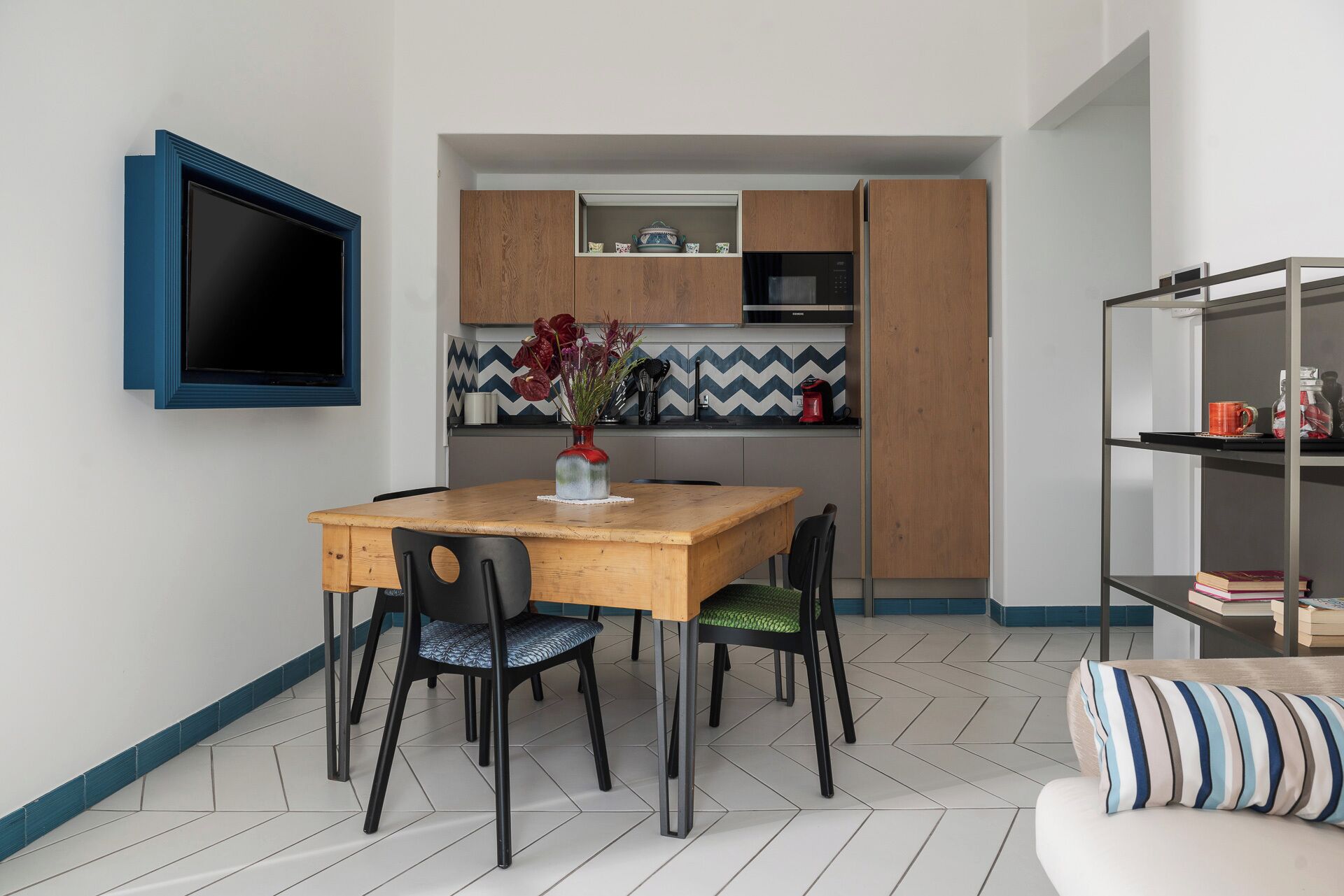 Een kleine keuken met een houten tafel, stoelen en een aan de muur bevestigde televisie.